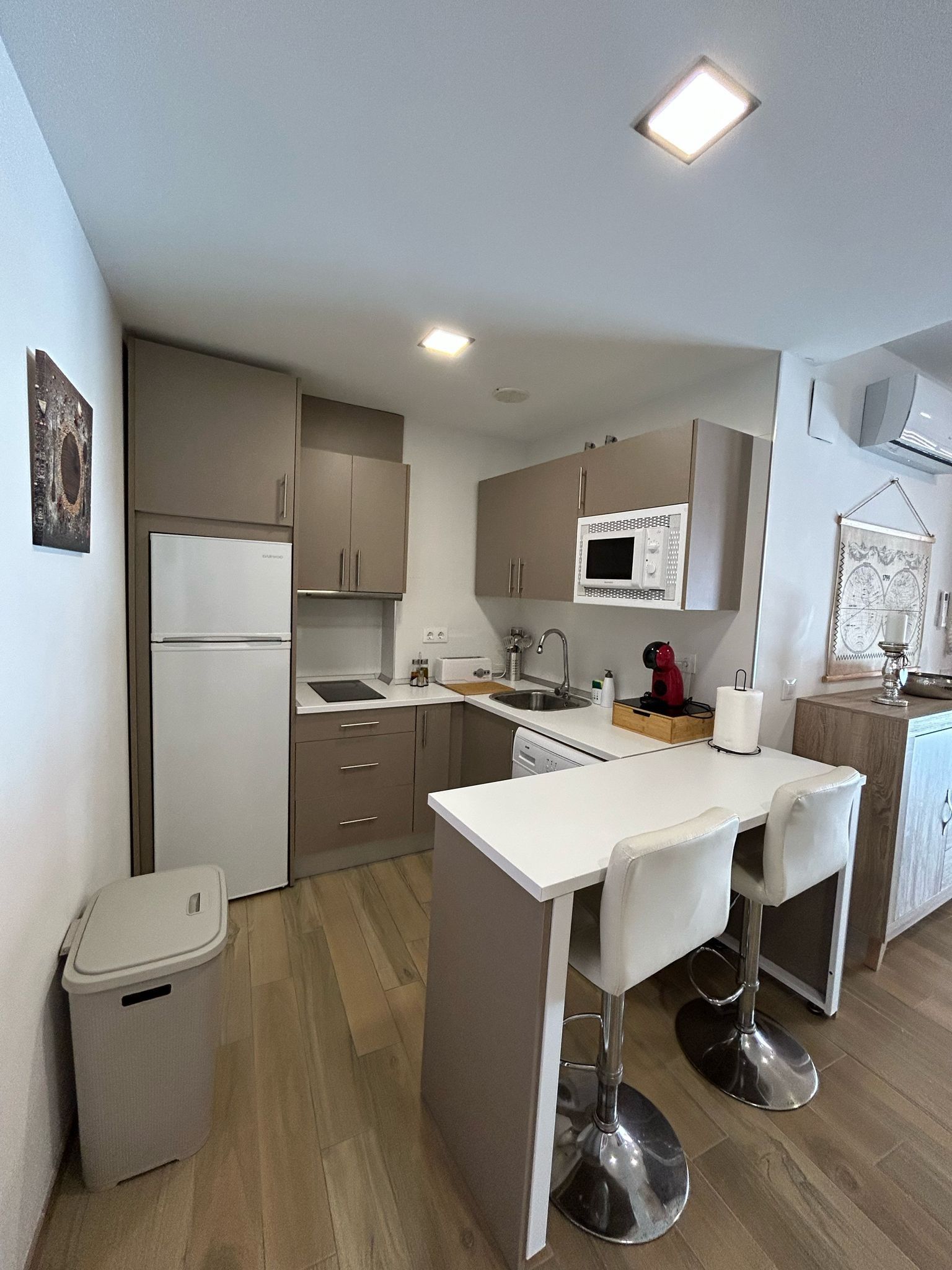 Una cocina compacta con electrodomésticos modernos, un pequeño comedor y un cubo de basura.