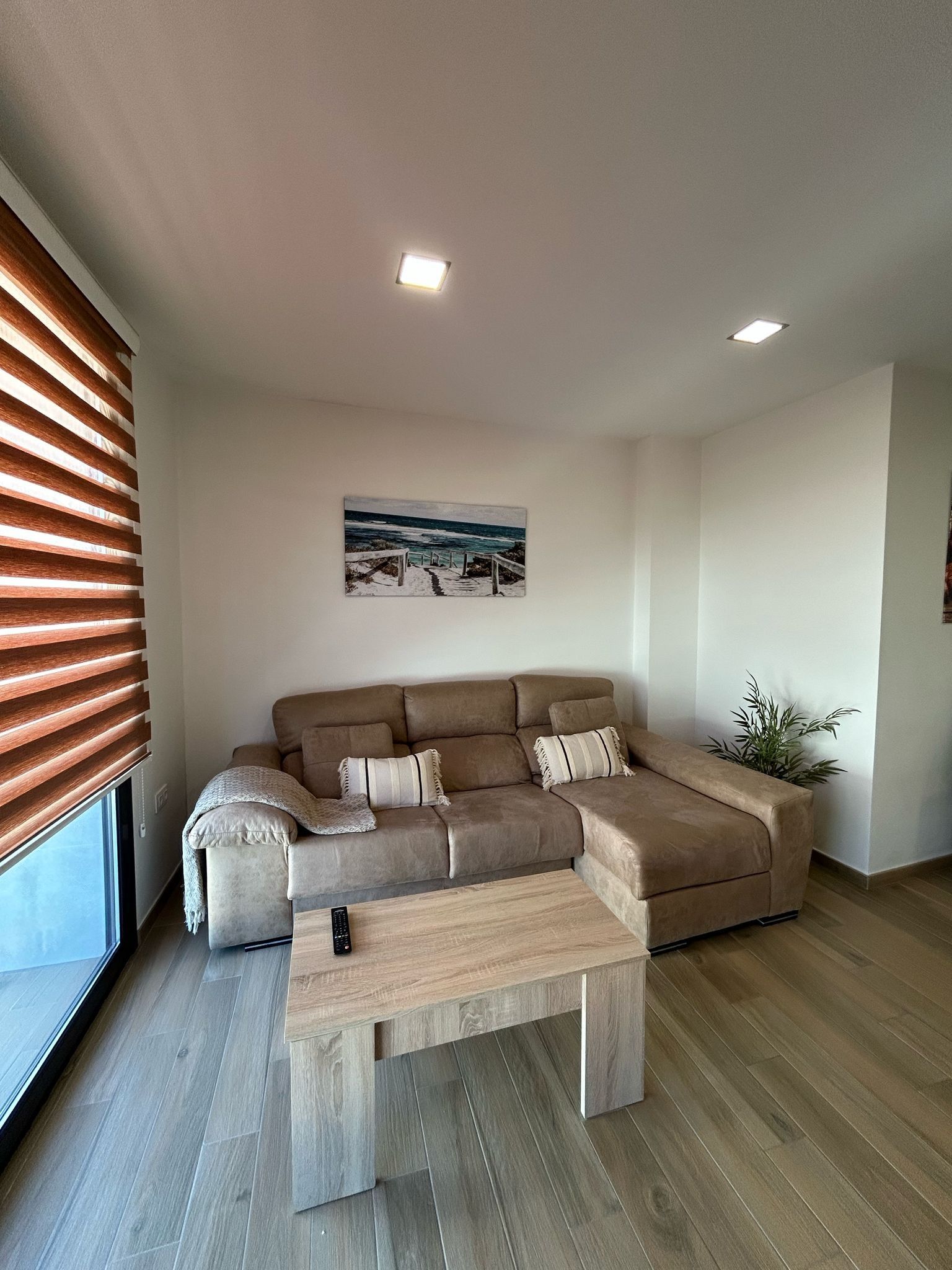 Una sala moderna con un sofá seccional, una mesa de centro y un cuadro de una playa.