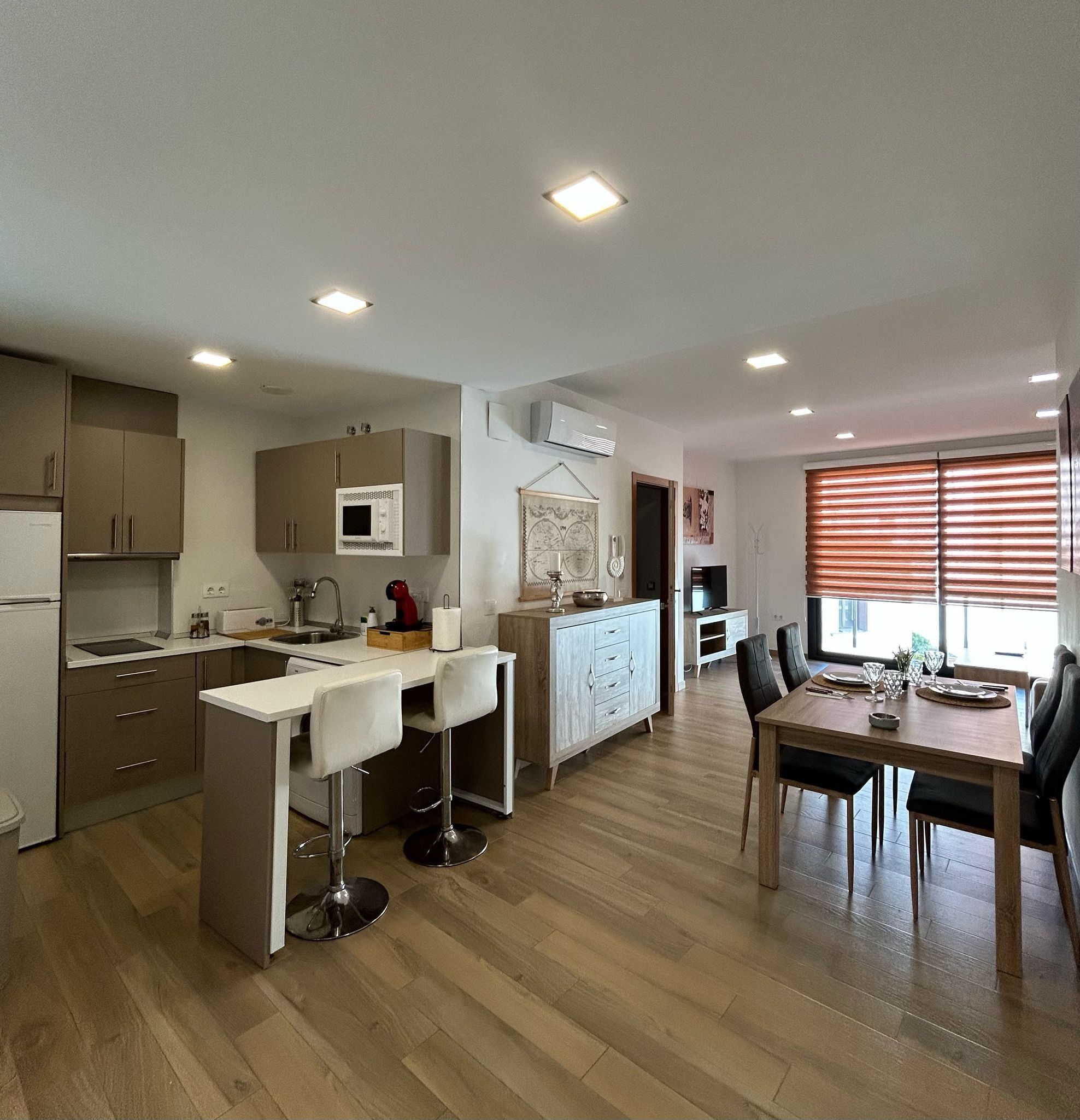 Una cocina moderna con comedor, suelo de madera y luces empotradas en el techo.
