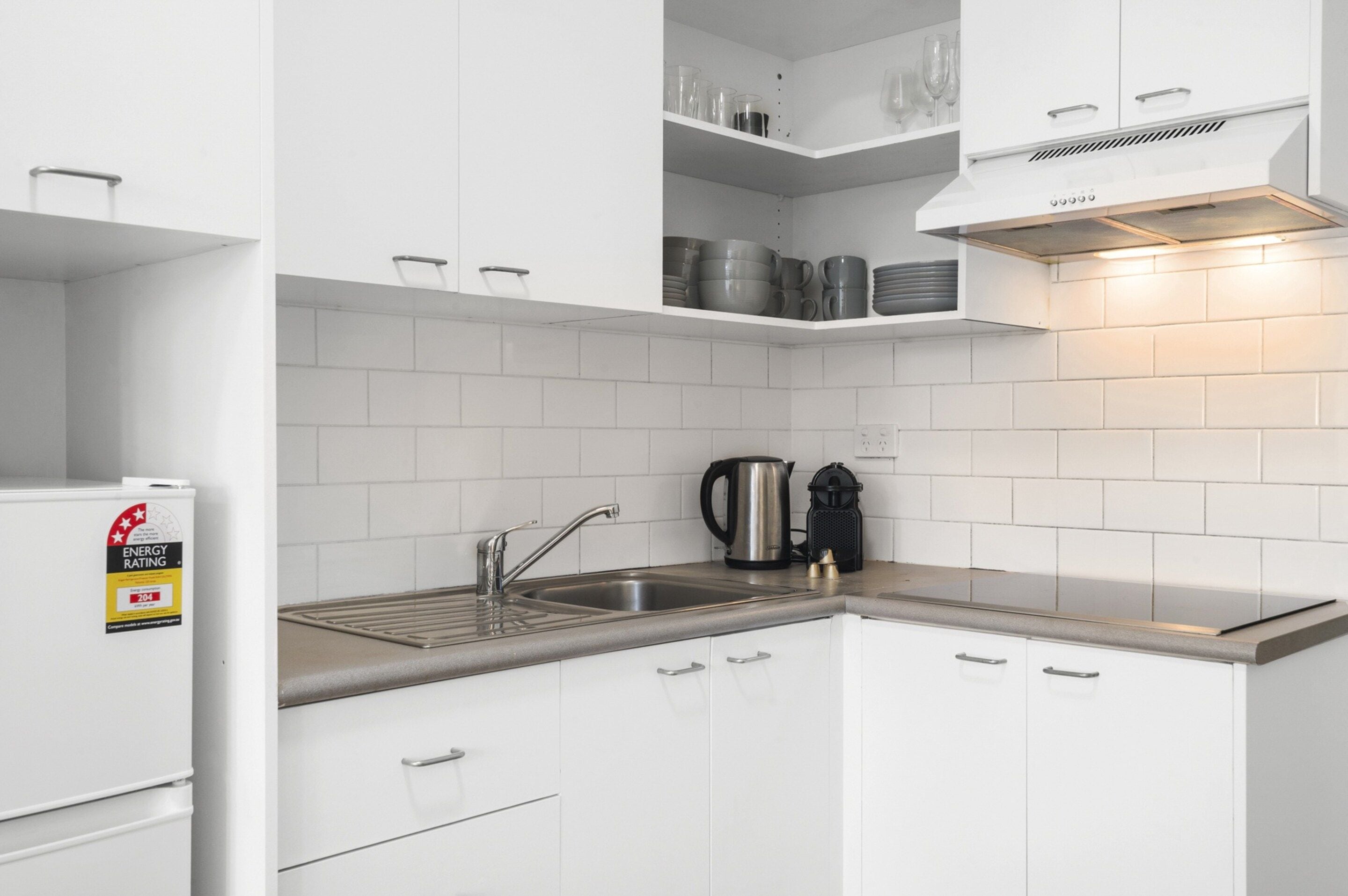 Una cocina moderna con armarios blancos, un lavamanos de acero inoxidable y una tetera.