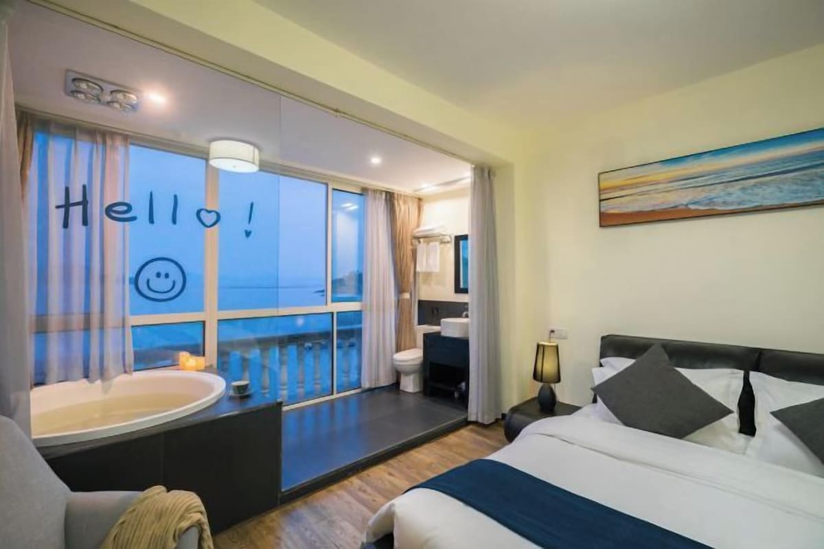 Una habitación de hotel con un ventanal grande, una bañera, una cama y un cuadro en la pared.