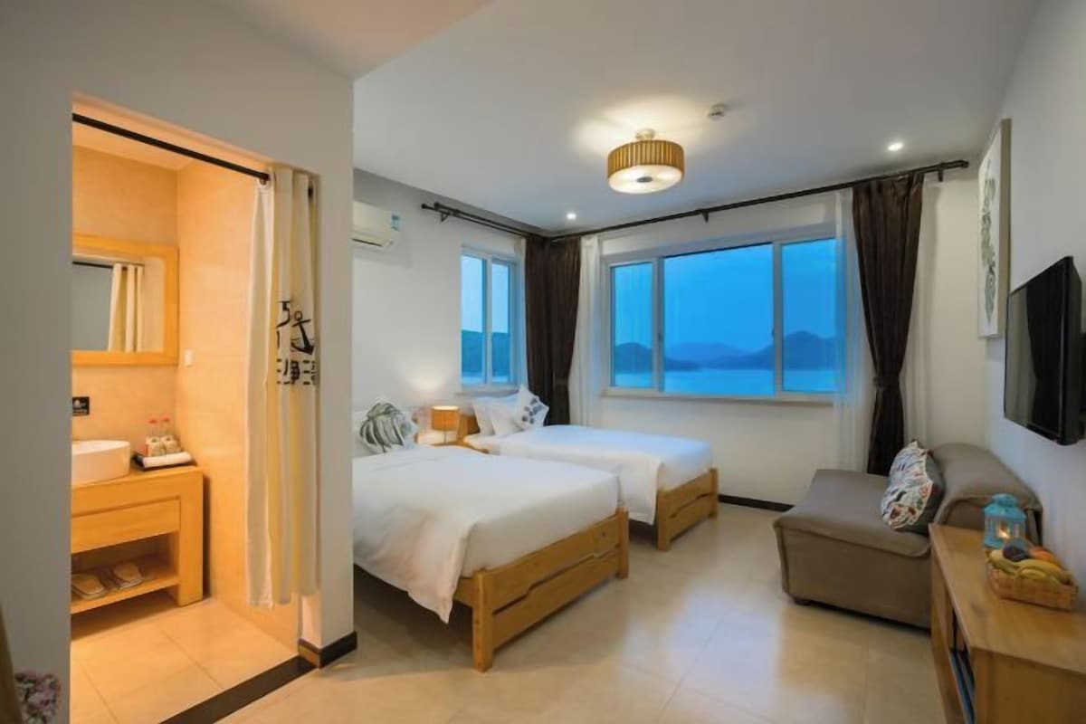 Habitación de hotel con dos camas, un sofá, un televisor y un baño con lavabo y espejo.