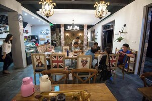 A restaurant interior with wooden tables and chairs, a chandelier, and a counter with food items.