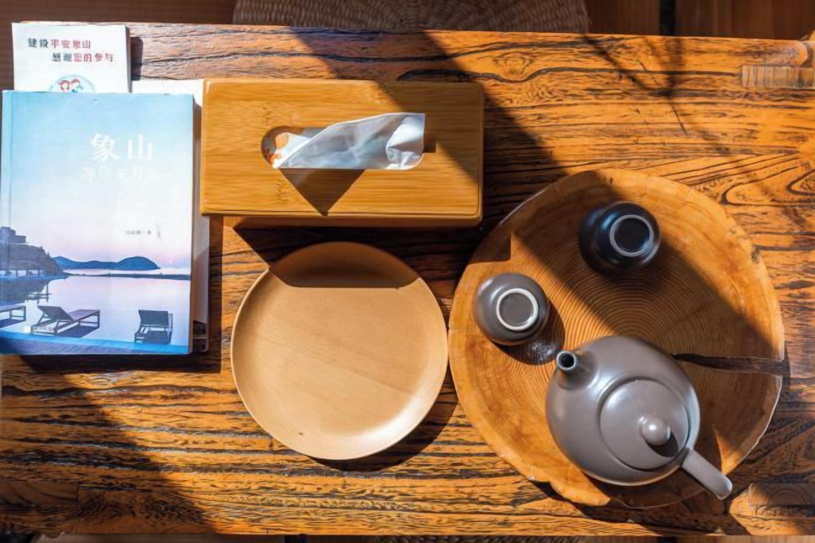 Une table en bois avec un livre, une boîte de mouchoirs, une assiette et une théière.