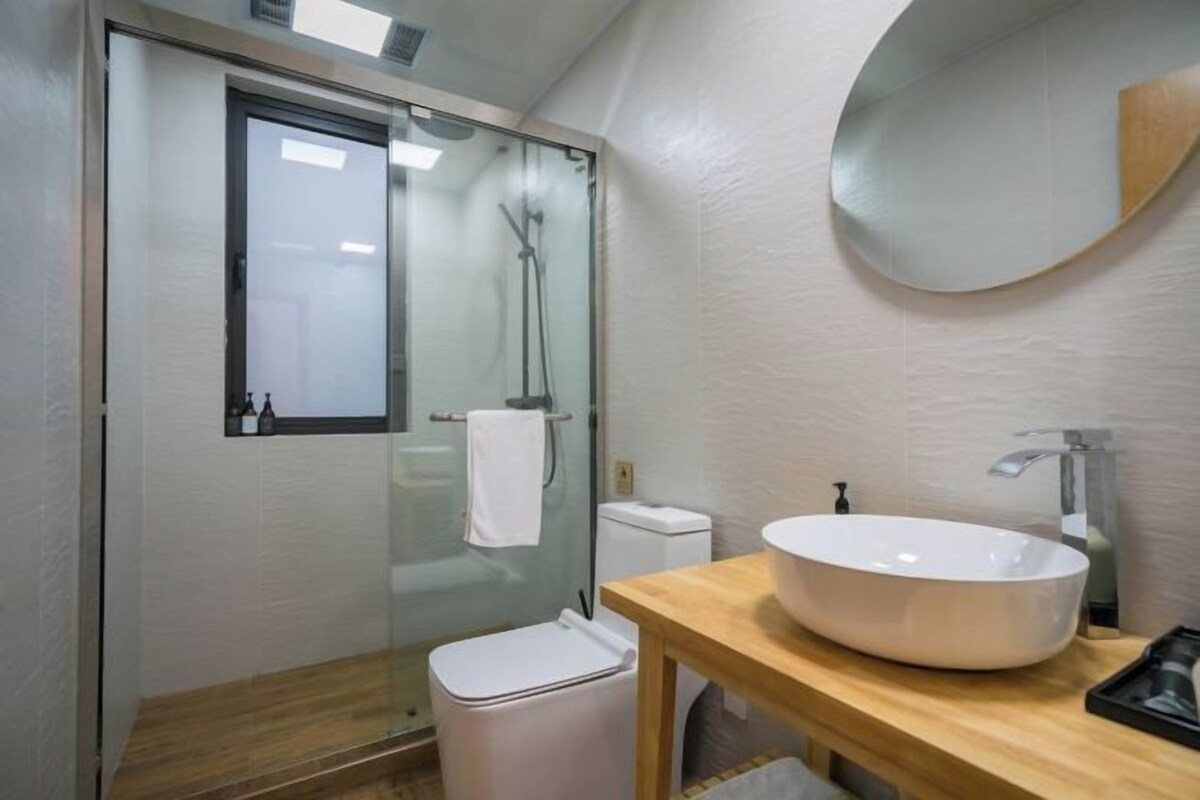 A modern bathroom with a glass shower enclosure, a white toilet, and a wooden vanity with a large sink.