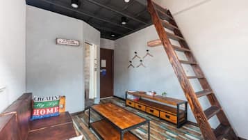 Quarto com beliche, um banco de madeira, uma mesinha, escada e prateleira na parede.