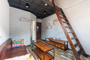 Une pièce avec un lit en mezzanine, un banc en bois, une petite table, une échelle et une étagère fixée au mur.