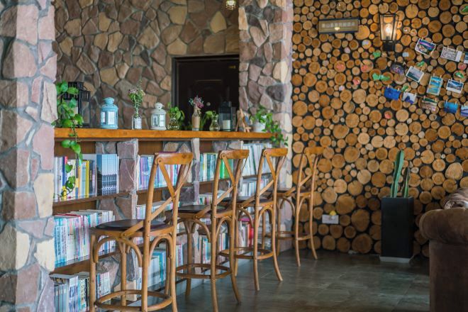 Interior rústico com parede de pedra, balcão de madeira e lenha empilhada.