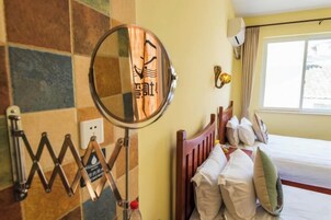 Habitación de hotel con cama, almohadas, un espejo, un calentador de pared y una ventana.