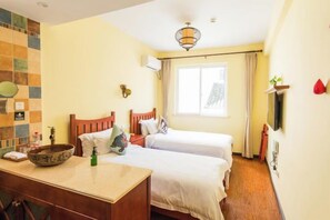 Habitación de hotel con dos camas, un escritorio con un frutero, un espejo y una ventana con cortinas.