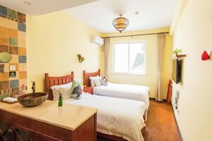 Habitación de hotel con dos camas, un escritorio con un frutero, un espejo y una ventana con cortinas.