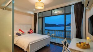 A bedroom with a bed, a table with a fruit basket, and a balcony with a view. - Shatang Jingwan Inn (Xiangshan)