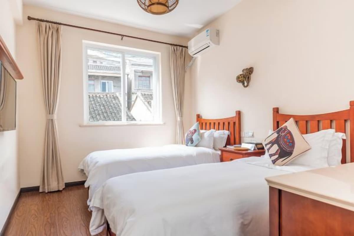 Habitación de hotel con dos camas, cabecero de madera, mesita de noche y ventana con cortinas.