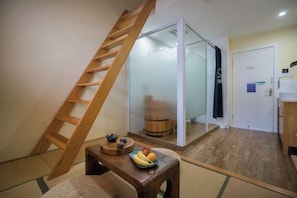 Une pièce avec une échelle en bois, une petite table sur laquelle sont disposés des fruits, et une porte coulissante qui donne sur une autre pièce.