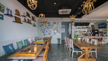 Un restaurante con largas mesas y sillas de madera, una pared decorada con fotografías enmarcadas e iluminación colgante.