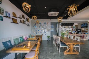 Un restaurante con largas mesas y sillas de madera, una pared decorada con fotografías enmarcadas e iluminación colgante.