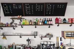 Zona de bar con estantes llenos de botellas y vasos, una máquina de café y un menú en una pizarra.