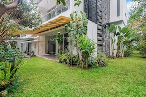 Ein modernes Haus mit überdachter Terrasse, üppigem Rasen und verschiedenen Pflanzen.