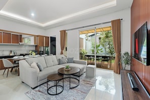 A modern living room with a grey sofa, a coffee table, and a dining area with a table and chairs.