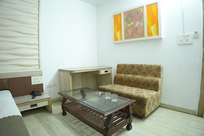 A room with a bed, a wooden coffee table, a patterned sofa, a desk, and two wall-mounted paintings. - Hotel Smriti Star (Bhopal)