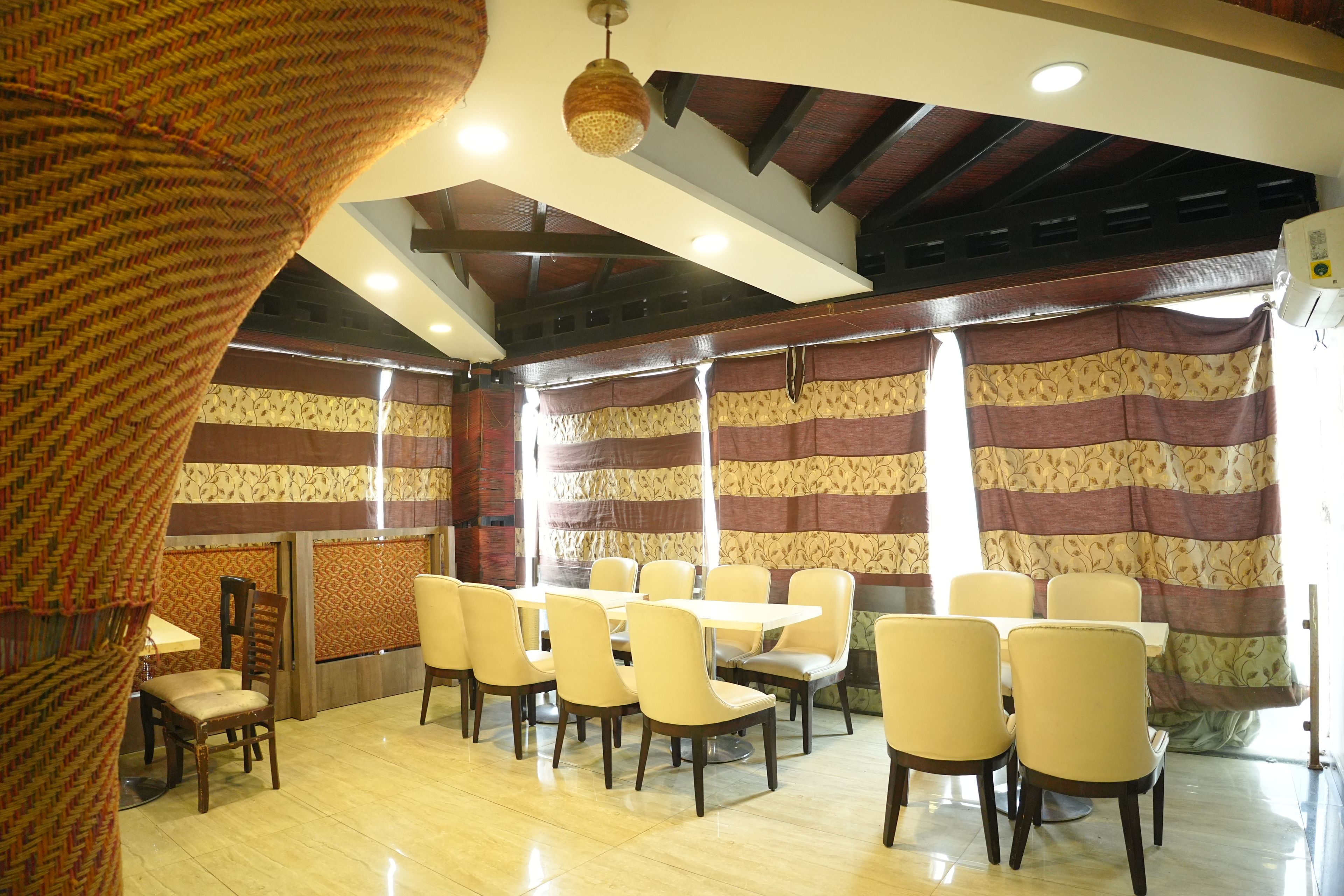A room with a high ceiling, patterned curtains, and a row of yellow chairs and tables.