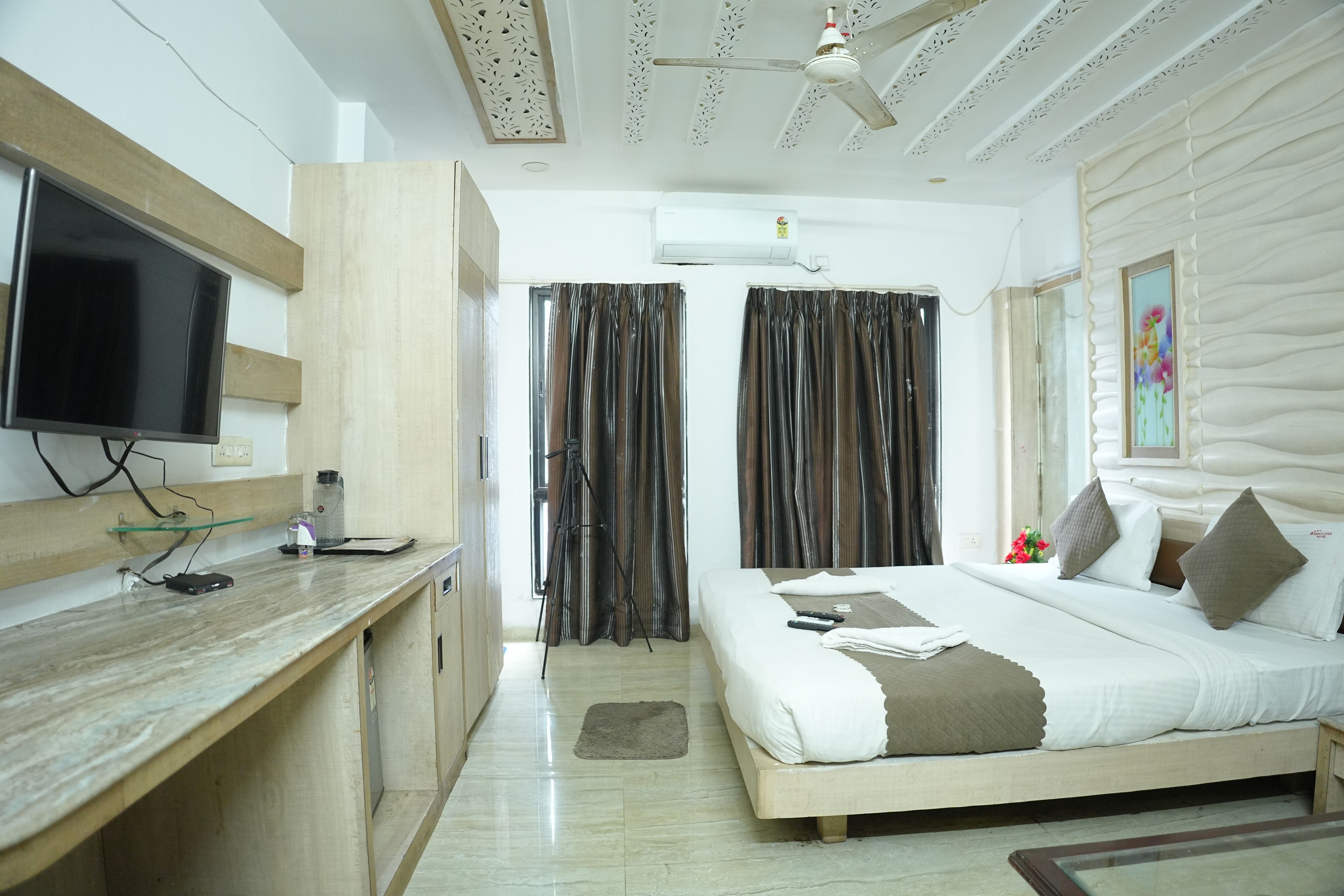 A hotel room with a bed, a desk, a television, and a ceiling fan.