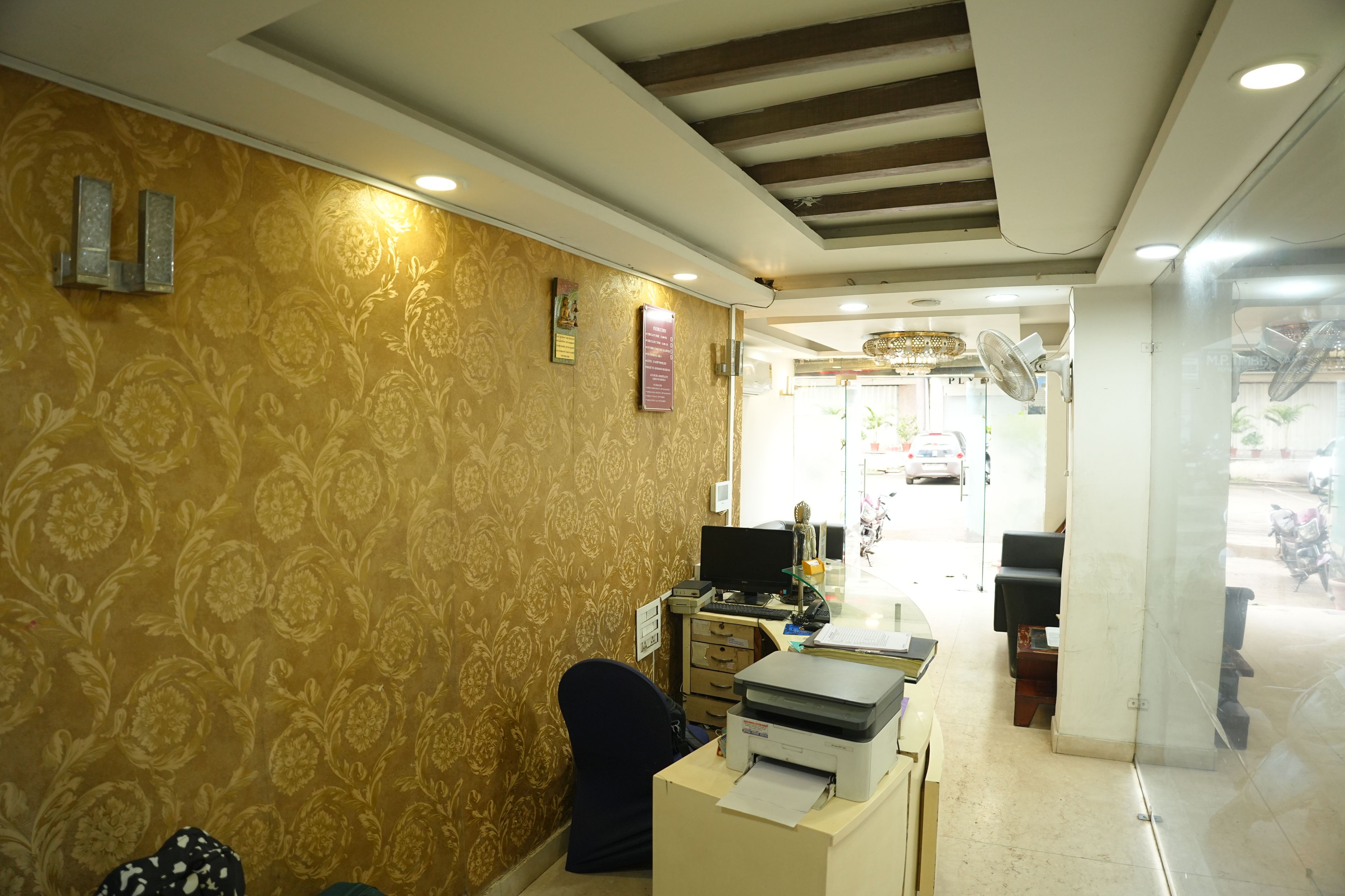 A reception area with a patterned wall, a desk with a computer, a printer, and a chair.