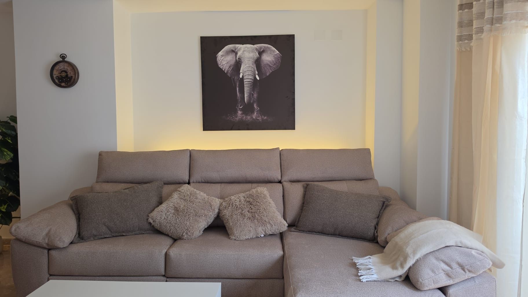 Ein Wohnzimmer mit einer Couch, Kissen, einer Wanduhr und einem gerahmten Bild.