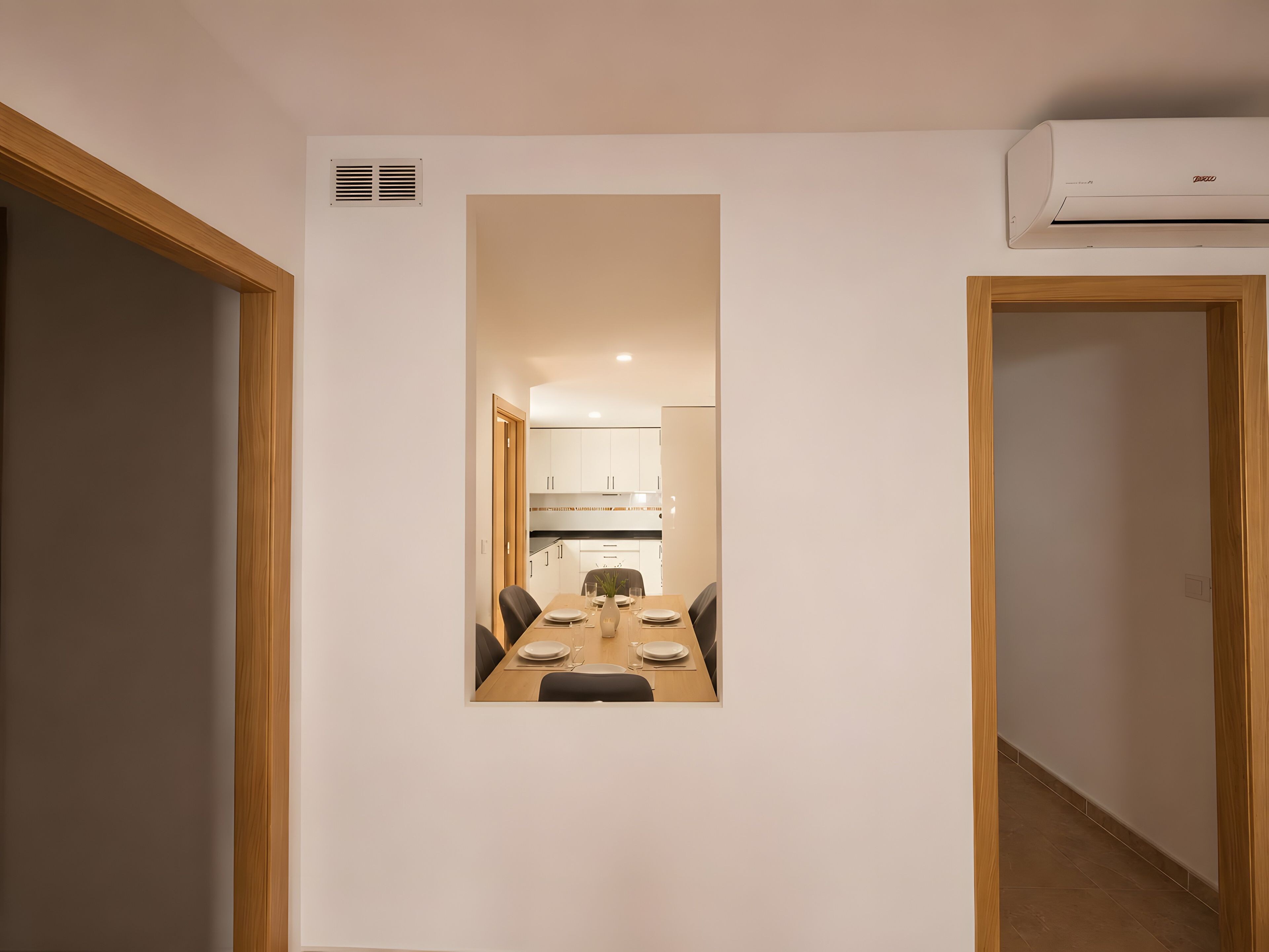 A hallway leading to a dining area with a table set for two, a kitchen visible through an open door, and an air conditioning unit mounted on the wall.