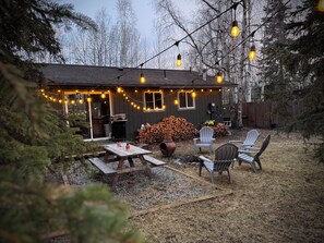 A rustic cabin with a deck, outdoor seating, and string lights. - Alaska Adventure Basecamp • Sleeps 6 • 
• 3BR / 2Ba • Yard + Fire Pit (Anchorage)