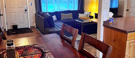 A dining area with a wooden table and chairs, a kitchen with wooden cabinets, and a living area with a sofa and a TV.