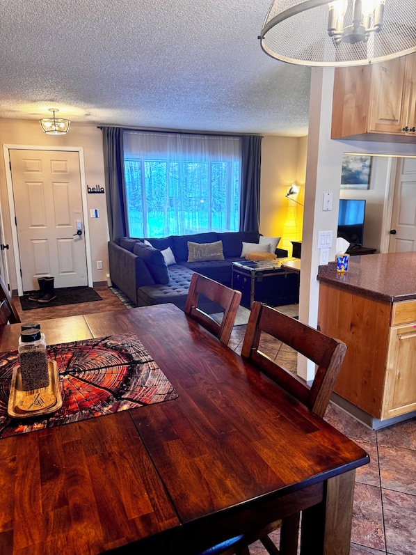 A dining area with a wooden table and chairs, a kitchen with wooden cabinets, and a living area with a sofa and a TV.