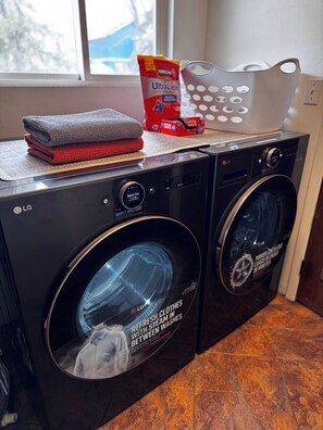 A front-loading LG washer and dryer set with a towel on top, a bag of laundry detergent, and a basket. - Alaska Adventure Basecamp • Sleeps 6 • 
• 3BR / 2Ba • Yard + Fire Pit (Anchorage)