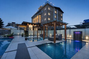 A modern hotel with a swimming pool, outdoor seating, and a covered patio area. - The Platinum Grand Mamta (Srinagar)