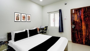 A hotel room with a bed, a desk, a chair, a window with curtains, and three framed pictures on the wall. - Super Townhouse Badangpet Crossway (Hyderabad)
