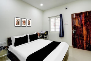 Habitació d'hotel amb llit, escriptori, cadira, finestra amb cortines i tres quadres penjats a la paret.