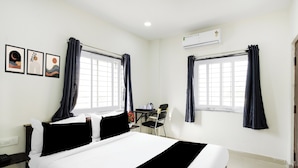 A hotel room with a bed, two windows with curtains, a desk with a chair, and wall art. - Super Townhouse Badangpet Crossway (Hyderabad)