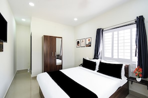 Habitació d'hotel amb llit, un armari, una finestra amb cortines i un televisor fixat a la paret.