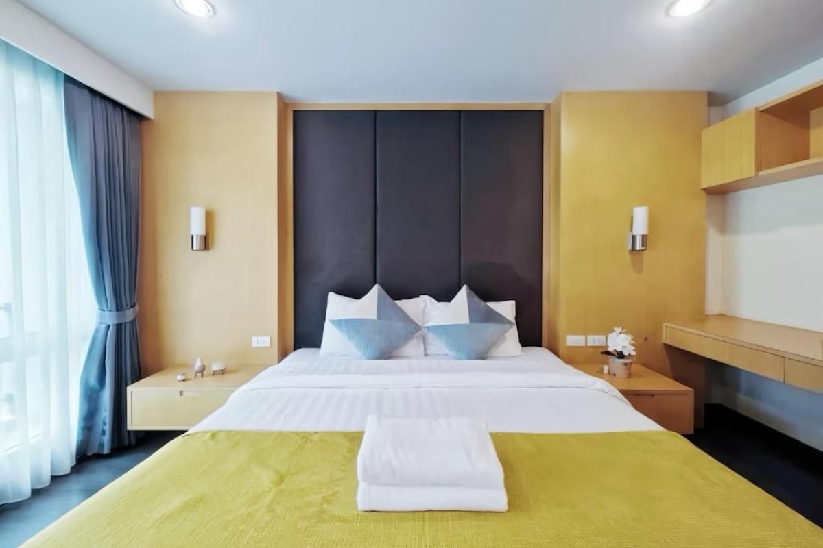 A hotel room with a bed, bedside tables, a nightstand, a desk, and a chair.