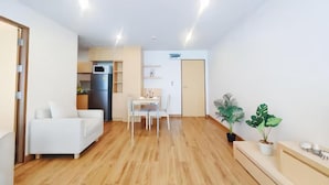 Un salon moderne avec un canapé blanc, une table à manger avec des chaises, et un coin cuisine à l’arrière-plan.