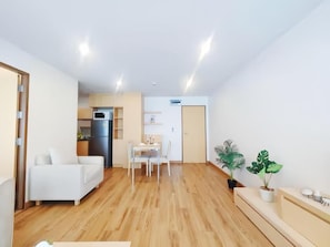 A modern living room with a white sofa, a dining table with chairs, and a kitchen area in the background. - Residence One Bangkok (Krung Thep Maha Nakhon)