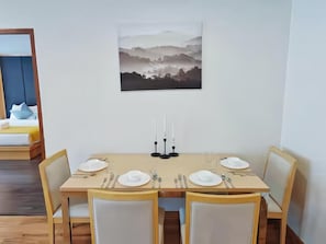A dining area with a table set for four, a painting on the wall, and a bed with pillows in the background. - Residence One Bangkok (Krung Thep Maha Nakhon)