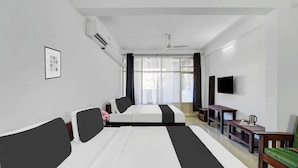 Habitación de hotel con dos camas, un televisor de pantalla plana, una mesita pequeña con un hervidor y una ventana con cortinas.