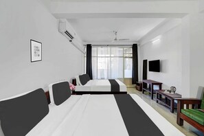 Habitación de hotel con dos camas, un televisor de pantalla plana, una mesita pequeña con un hervidor y una ventana con cortinas.