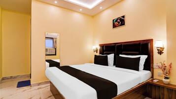 Una habitación de hotel con una cama grande, televisión, aire acondicionado instalado en la pared y una mesita de noche con una lámpara y un florero.