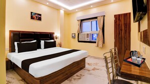 A hotel room with a bed, a desk with a kettle, a chair, an air conditioning unit, and a TV mounted on the wall. - Townhouse Puri Sea Beach (Puri)