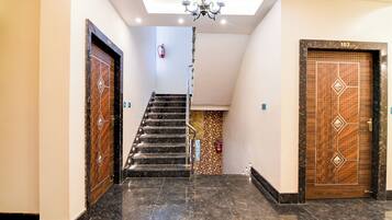 Un pasillo con piso de mármol, una escalera y dos puertas decoradas.