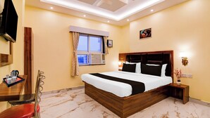 A hotel room with a bed, a desk, a chair, a window, and a wall-mounted TV. - Townhouse Puri Sea Beach (Puri)