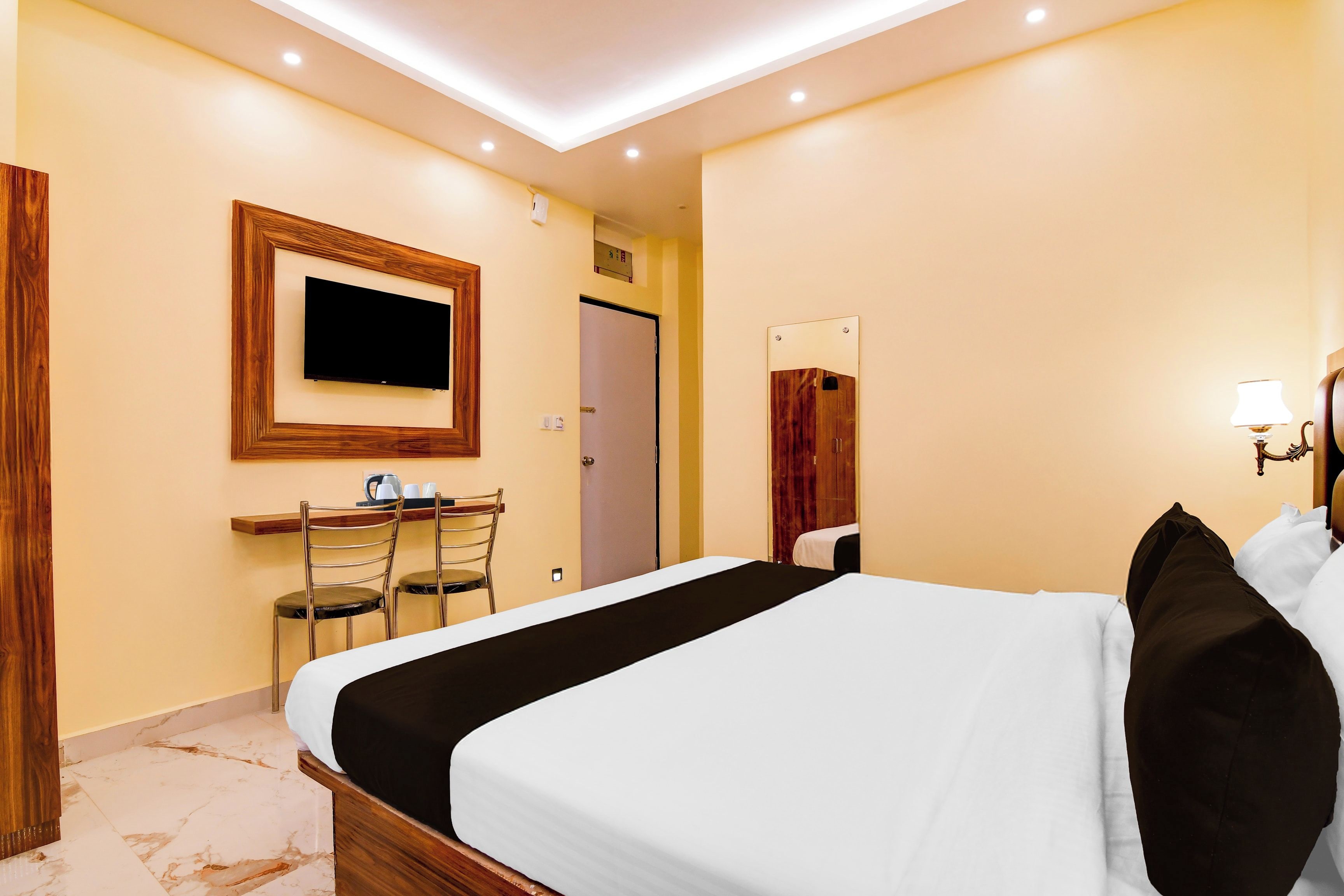 A hotel room with a bed, a desk with chairs, a television, a mirror, and a lamp.