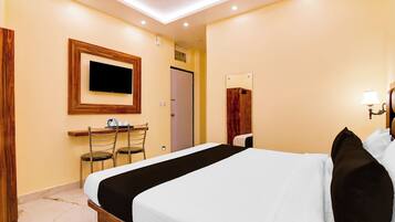 A hotel room with a bed, a desk with chairs, a television, a mirror, and a lamp.
